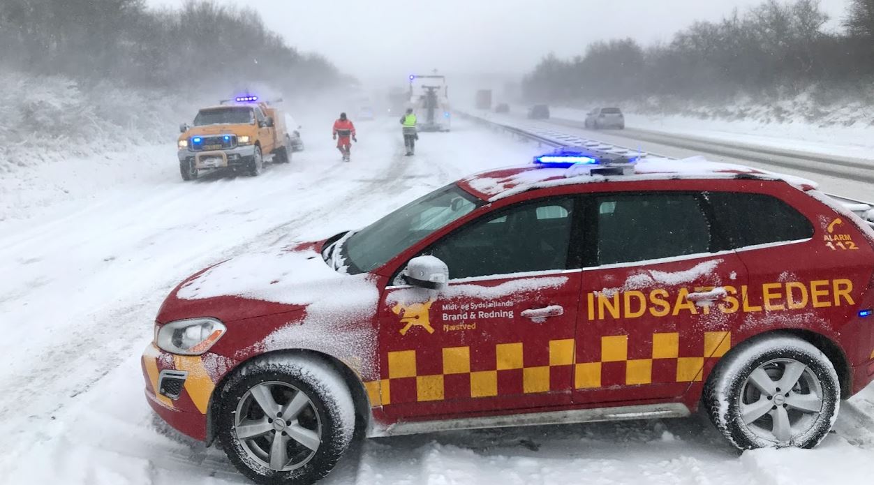 Rød indsatslederbil der holder i vejkanten, med udrykning, under snestorm.